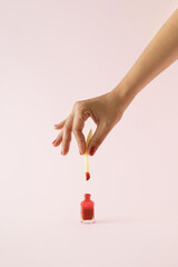 Hand dipping french fried potato in red nail polish on pink background. Minimal concept.