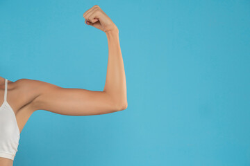Young woman's bent arm , showing bicep. Isolated on blue background.