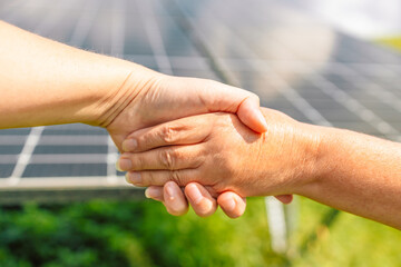 Close up view of shaking hands after discussion on background of solar panels.