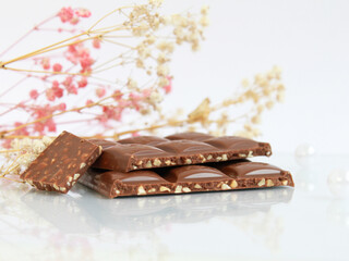 Pieces of milk chocolate with nuts isolated on white mirror background with flowers