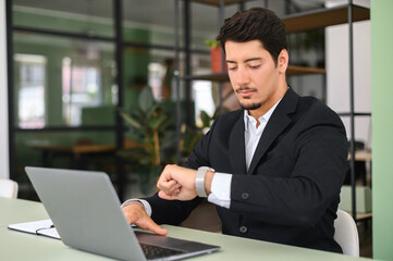 Busy young latin male entrepreneur or employee in formal wear sitting in office and working on...