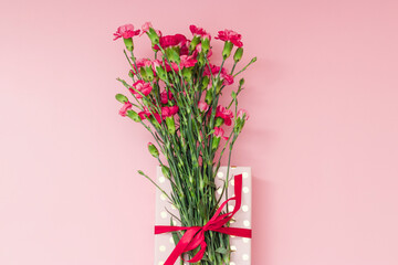 Red mini carnation and gift box. Concept of giving present at mother's day as surprise, flat lay, top view On pink Background