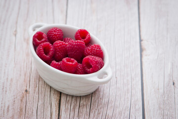 Harvest of Fresh ripe farm raspberry on the table, on wooden background in white plate. Top view, copy space. Flat lay with space for text.