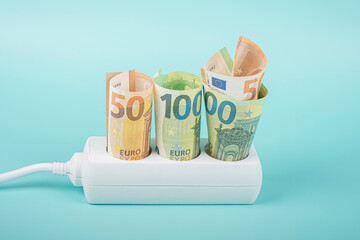 Euro money banknotes plugged in power strip extension cord on light blue background. Electricity...