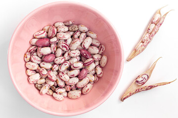 Cranberry beans on an isolated white background. Cranberry beans inside and outside the pink bowl. - obrazy, fototapety, plakaty