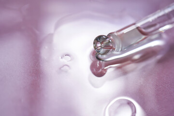 Dropper with serum or cosmetic oil on a pink background.