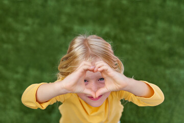Pretty blonde child girl showing sign of love heart from fingers hands. Top view