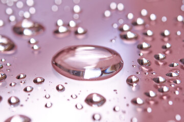 A large drop and splashes of micellar water on a pink background.