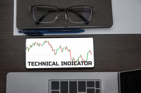 Technical indicator text in phone. Top view of chart in the phone on the table near laptop, notepad, and glasses.