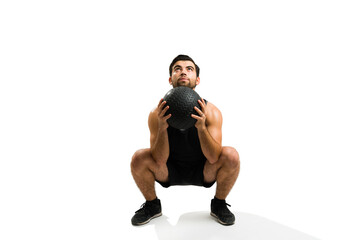 Fitness man using a slam ball while doing squats in cross training