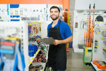 Retail worker looking cheerful while doing inventory at the hardware store - obrazy, fototapety, plakaty