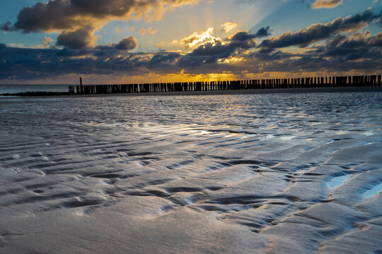 A dramatic sunset over a sandy beach and the North sea in the Netherlands seen from the beach in Zoutelande, Zeeland  with the typical wooden breakers for the waves during high water