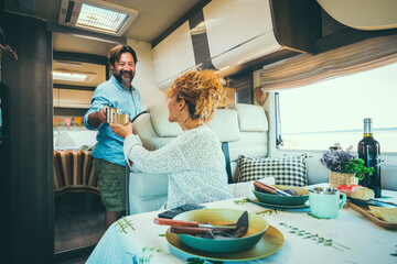 Couple living off grid inside a modern luxury camper van and enjoy travel lifestyle. People on vacation with home vehicle. Concept of van life for man and woman having lunch inside a motor home - obrazy, fototapety, plakaty