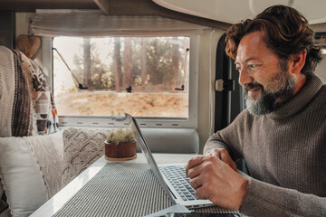 One man work on laptop inside a camper van sitting at the desk table. Modern online connection job...