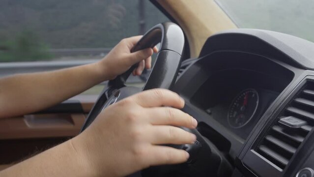 Holding the steering wheel of the car.
Hands holding the steering wheel on the console of the moving car turn on the signal and window water.
