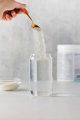 Collagen powder is poured into a glass of water from a golden spoon on a gray background. The...