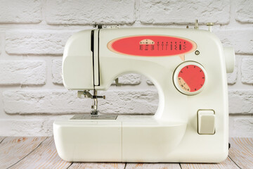 Modern multi operation sewing machine, assortment of different stitches for decorating clothes on table in tailor's workshop or atelier on white brick background.