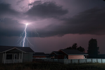 Thunderbolt over the house in the village and dark stormy sky on the background