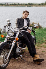 Fototapeta na wymiar Stylish handsome biker is sittind and chilling on his motor bike outdoors