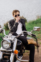 Fototapeta na wymiar Stylish handsome biker is sittind and chilling on his motor bike outdoors