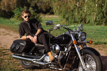 Naklejka na ściany i meble Young handsome male biker is sitting on his motor bike outdoors at the lake background