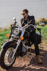 Young handsome male biker is sitting on his motor bike outdoors at the lake background