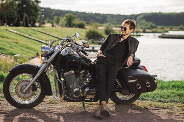 Fototapeta na wymiar Young handsome male biker is sitting on his motor bike outdoors at the lake background