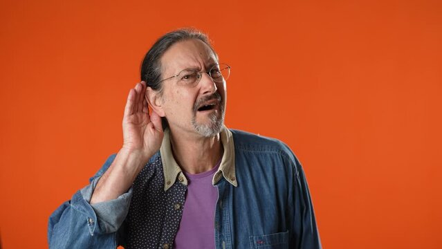 Man struggles to hear, having difficulty hearing, isolated on solid orange background studio portrait.