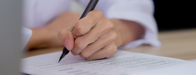 Closeup hands of doctor woman signing on document paper at clinic, close-up hands of physician...