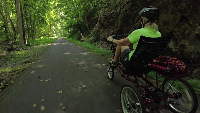 Elderly woman riding recumbent bike on a path on a sunny day in the forest.