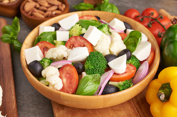 Greek salad or horiatiki with large pieces of tomatoes, cucumbers, onion, feta cheese and olives in white bowl isolated top view. Village salad with diced mozzarella, arugula, parsley and olive oil