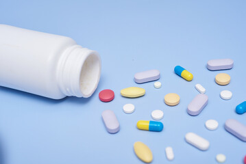 Pile of medical capsules pills in red and white color on blue background, top view for copy space. White medical pills and tablets spilling out of a drug bottle. Macro top down view with copy space.