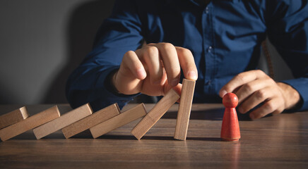 Male hand stopping wooden blocks from falling on human figure.