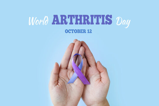 World Arthritis Day. Adult hands holding blue purple ribbon on blue background. RA rheumatoid arthritis illness disease.