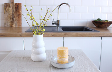 Modern white ceramic vase with yellow blooming Forsythia flowers on a vintage bench table. Scandinavian interior.