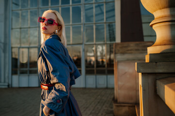Fashionable confident blonde woman wearing trendy rectangle sunglasses, stylish blue trench coat,...