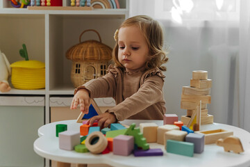 A little girl playing with wooden blocks on the table in playroom.  Educational game for baby and...