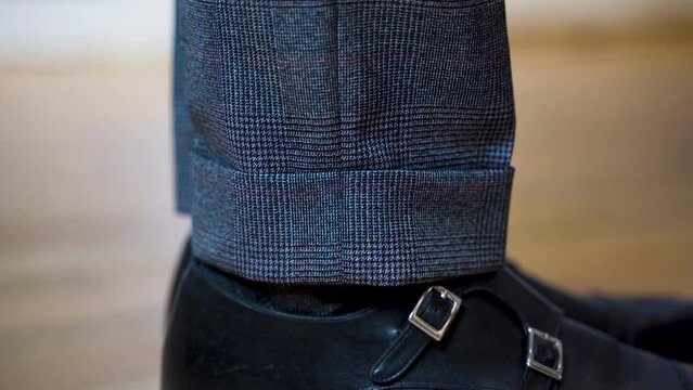 Side view close up of suit trousers cuff and patent shoes with straps.
