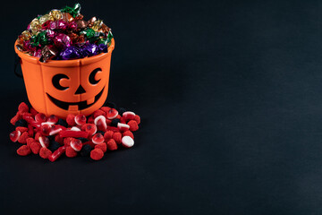 Halloween pumpkin shaped bucket full of candies against black background