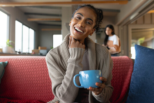 Portrait of smiling biracial mid adult woman with hand on chin and holding coffee cup on sofa