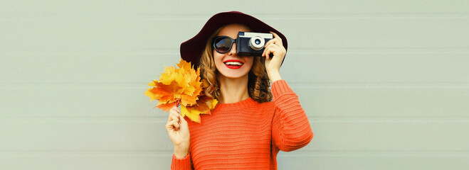Autumn portrait of happy smiling woman with film camera and yellow maple leaves wearing red sweater...