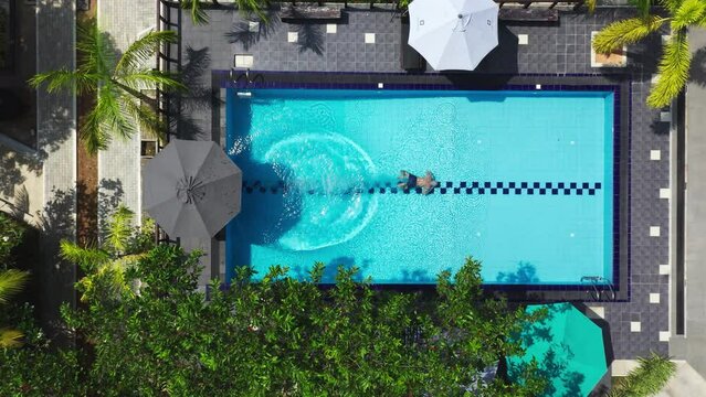 4K drone footage from great height man jumping into swimming pool and swimming. Relaxation, exotic resort, tropical villa concept.