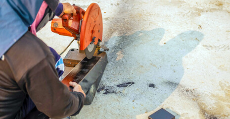 The worker in the work clothes uses an electric steel cutter. Cutting large steel bars at the construction site