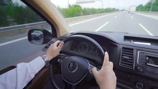 The interior of a moving vehicle.
Hands holding the instrument panel and steering wheel of the vehicle in motion on the road.
