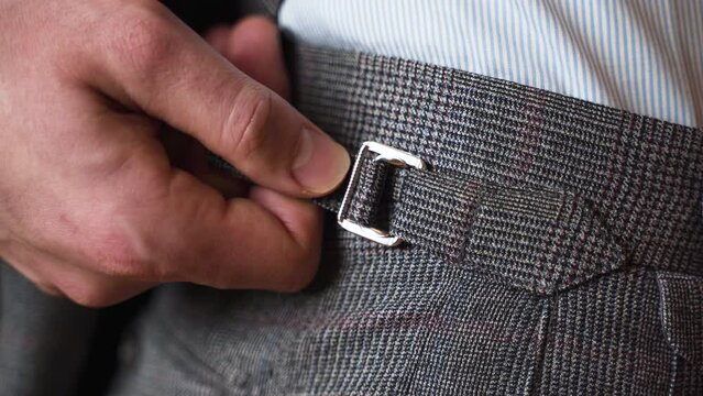 Tightening side adjuster on grey tweed suit trousers, close up.