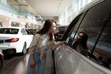 young woman dreamily looking at new cars in a car dealership