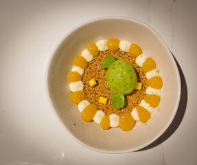 Passion fruit posset dessert with sesame crunch, coconut cream and coriander sorbet on a white dish