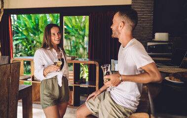 Cheerful Caucasian male and female with wine glasses smiling during positive date at home terrace, joyful couple in love 30 years old talking during recreation leisure for live communication together