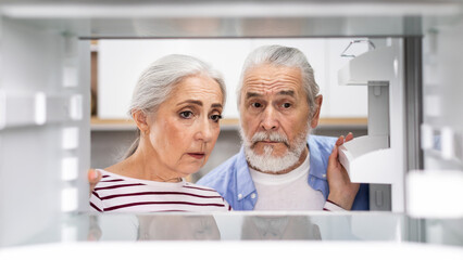 Crisis And Poverty. Upset Senior Couple Looking At Empty Shelves In Fridge