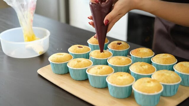 Young Caucasian woman cooks desserts in kitchen at home, process of cooking of cupcakes, filling with sweet filling, jam. Concept of small home business and entrepreneurship.